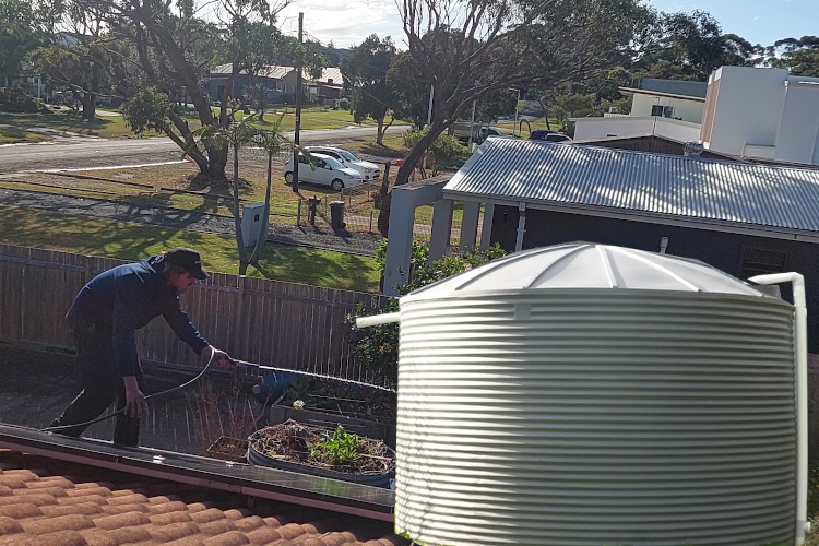 a ulladulla gutter cleaning service is rinsing out a rural property's gutters that rely solely on water tanks for all their water needs